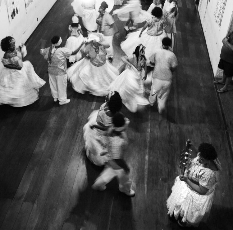 Dança Congada com giros e mulher tocando chocalho