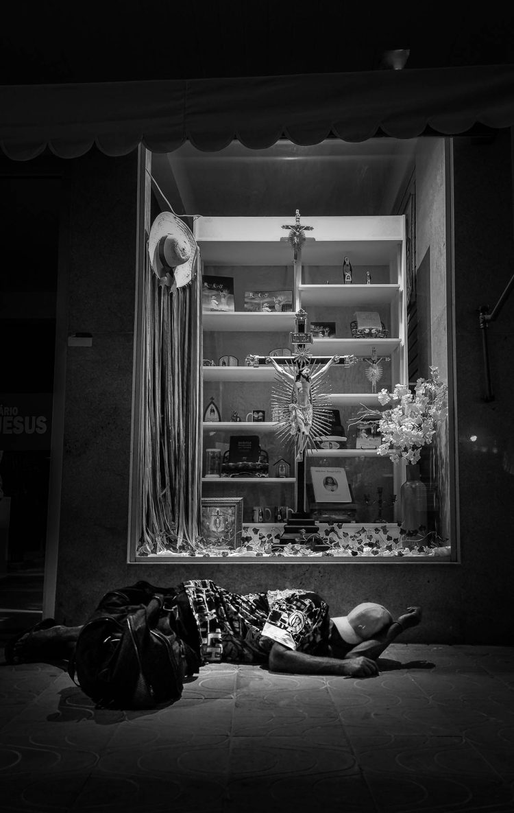 Um homem dormindo em frente à vitrine de uma loja.