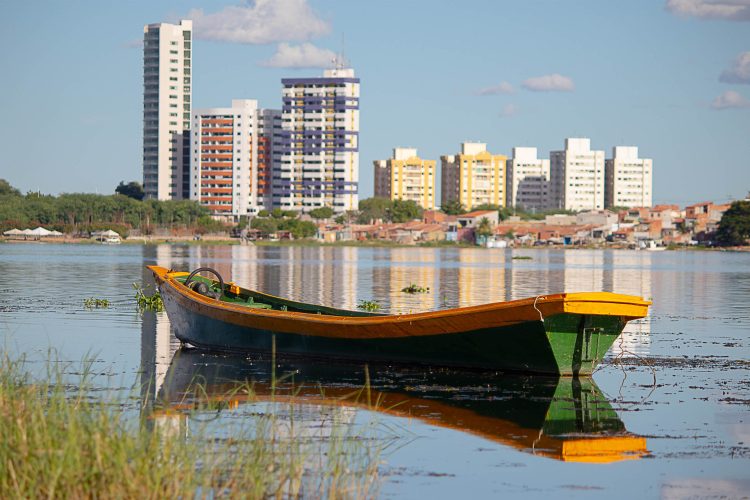 Entre a canoa solitária e os prédios ao fundo, o rio costura dois mundos que mal se olham. O reflexo na água une o que a margem separa: o urbano e o ribeirinho, o presente e o ancestral.