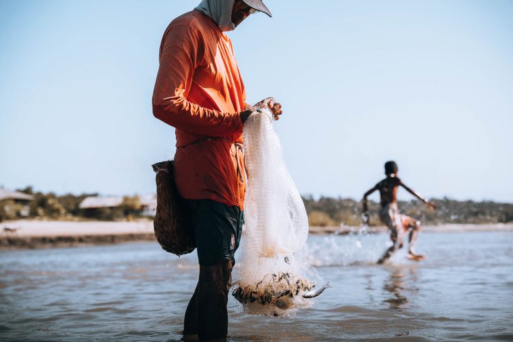 Rede Cheia
Rede artesanal cheia, pescador caminhando.n Ao fundo, criança brinca na mesma água onde ele trabalha. Mangue Seco é destino turístico, mas antes de ser cartão-postal, é fonte de sustento. Resultado concreto de quem pesca enquanto outros nadam.