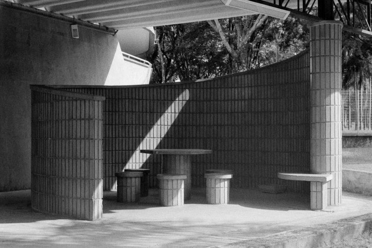 Abertura: o vazio como prelúdio do isolamento
A primeira fotografia, em preto e branco, é a única sem figuras humanas. Apenas bancos de concreto ocupam o quadro, imóveis e silenciosos. Ela estabelece o tom: o isolamento não começa
nas pessoas, mas na própria cidade; em seus espaços projetados para conter corpos que
raramente encontram repouso.