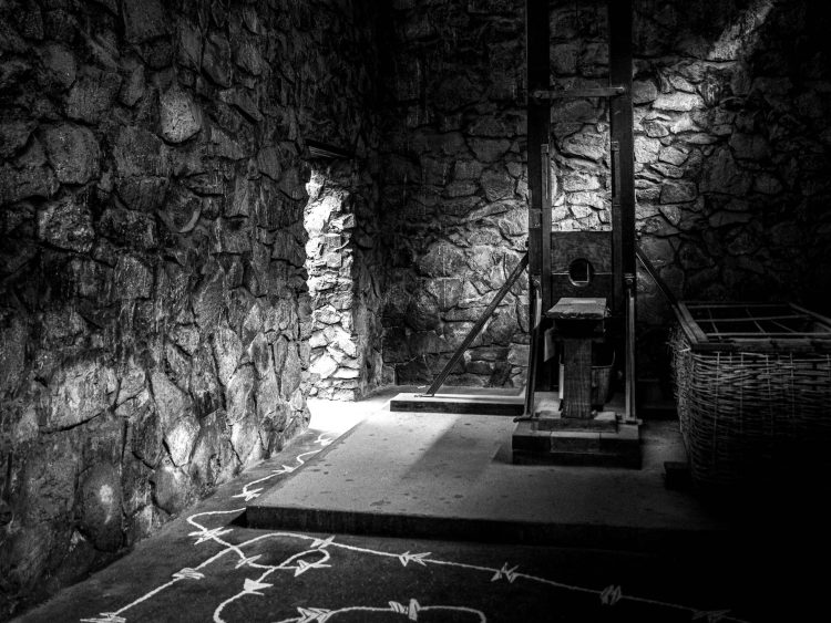 Chalk Orders (Ordens de Giz) 
Linhas traçadas no chão coreografam corpos. A segurança vira roteiro; a obediência, caminho. A moldura ancora o peso da guilhotina — madeira e ferro — contra marcas no piso que parecem rotas riscadas ou sombras de arame farpado. A luz difusa achata o espetáculo em testemunho; o espaço negativo ao redor do aparato soa como um fôlego contido.
Factual — Guilhotina exposta no War Remnants Museum, Saigon (Ho Chi Minh City, Vietnã). Relíquia colonial e de guerra que encarna a crueldade institucional imposta ao Oriente.
War Remnants Museum, Saigon (Ho Chi Minh City), Vietnã, 2/12/2013