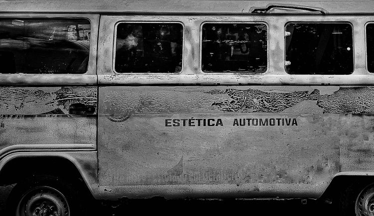 A Ironia da Ferrugem. A deterioração atinge os símbolos de nossa mobilidade. Uma crítica social gravada na lataria corroída: a promessa de "Estética Automotiva" contrasta ironicamente com a desintegração do metal. A ferrugem atua como a assinatura do tempo, documentando o ciclo de consumo.