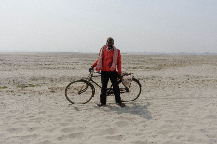 A working-class man commuting through the silt desert to reach his workplace, dragging his cycle along.